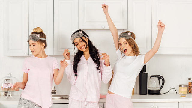 Beautiful Multicultural Girls In Sleeping Masks Dancing And Having Fun In Kitchen During Pajama Party