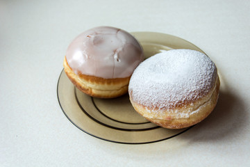 Two donuts with icing and sugar powder on a glass plate