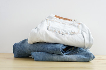Stack of jeans in different colors on wooden table texture and white background isolation.