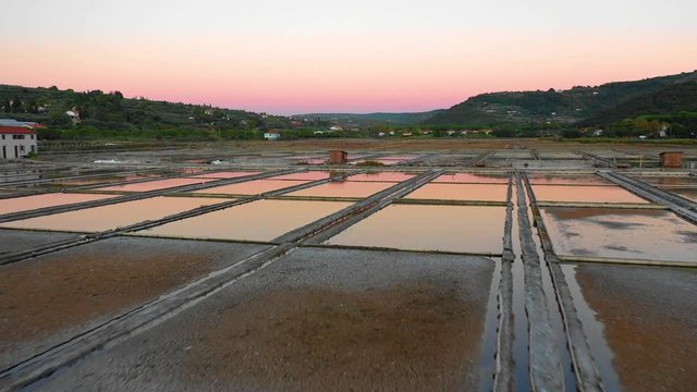 Aerial view of drone flying low with nice sunset reflection vibrant colors over the small salt pans where salt from see water is produced in Slovenia, Secovlje
