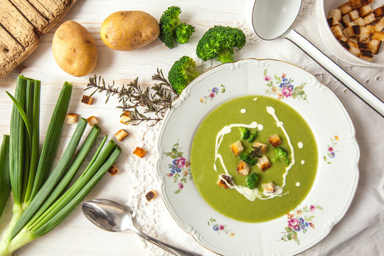 Spring detox broccoli green cream soup with potatoes and vegan cream in bowl on bright wooden board over white background, top view. Clean eating, dieting, vegan, vegetarian, healthy food concept