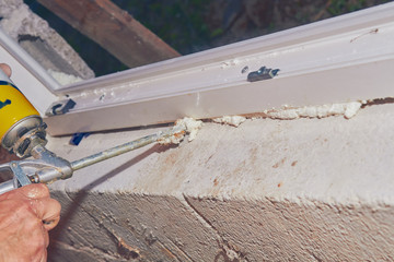 Construction worker puts expandable foam on the PVC window for insulation.