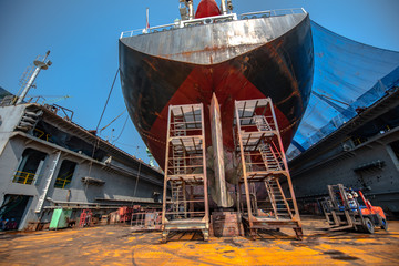 aft of commercial general bulk cargo ship in floating dry dock yard, sitting on concrete supporters...