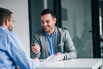 Smiling businessman giving pen to a client for signing a contract.