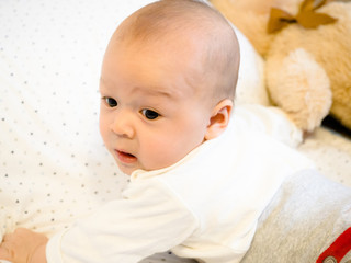 Cute 3 months old old mixed race Asian Caucasian boy looking happy wondering face, tummy time on belly on the bed, healthy child baby boy. Half Thai half Polish.