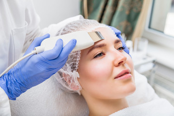 Cosmetologist makes ultrasound cleaning procedure in salon