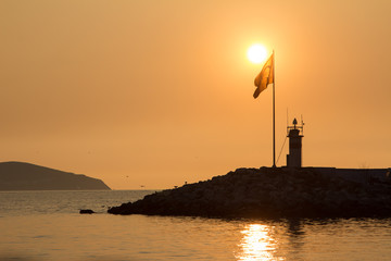 Fototapeta premium Beautiful sunset at Bostanci Pier. A Turkish flag is backlit by the setting sun.