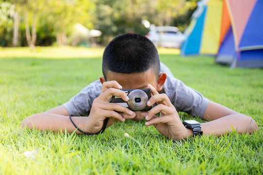Little boy taking a picture with a camera while lying on the grass in the park on a sunny summer day.