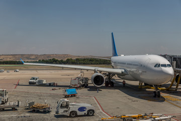 Fototapeta na wymiar Commercial airplane parked on a runway preparing to fly, next to luggage transport vans and other vehicles