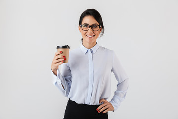 Image of young secretary woman wearing eyeglasses drinking coffee from paper cup in the office, standing isolated over white background