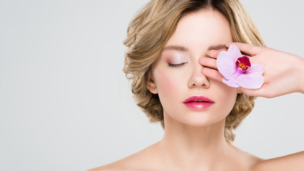 beautiful tender girl holding flower near closed eyes isolated on grey