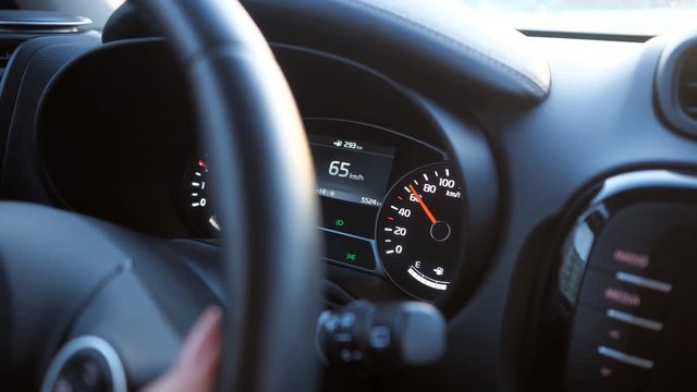 woman drives a car - closeup of hand on the steering wheel and speedometer