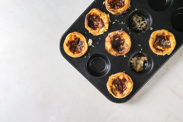 Traditional Portuguese egg tart dessert Pasteis Pastel de nata in black baking tray over white marble background. Flat lay, space