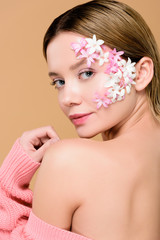 pretty girl with flowers on face looking at camera isolated on beige