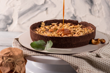 Cocolate tart with peanuts and caramel on the white wooden background