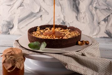 Cocolate tart with peanuts and caramel on the white wooden background