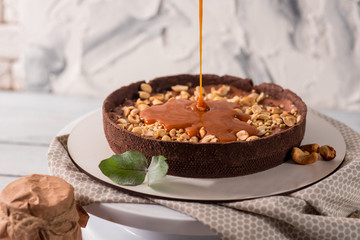 Cocolate tart with peanuts and caramel on the white wooden background