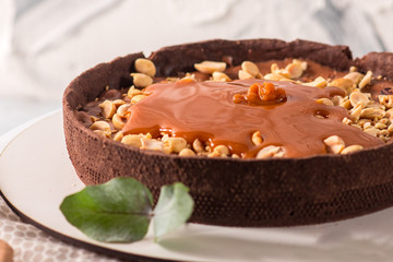 Cocolate tart with peanuts and caramel on the white wooden background