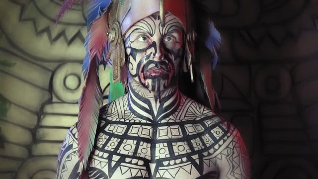 Ancient aztec warrior with crossed eyes, blood around his mouth and body paint on his body