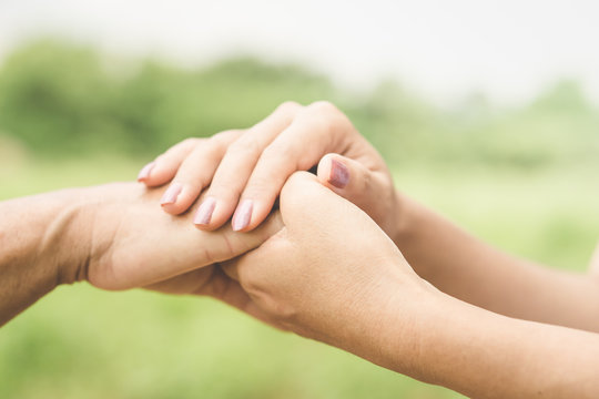 close-up of a daughter holding her mother's hand outdoors over nature background 