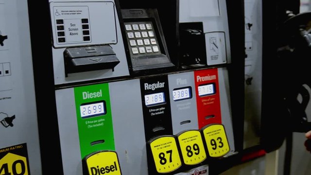 A young attractive brunette lifts the nozzle off of a gas pump and selects the octane before turning to fuel up her vehicle on a cold winter night