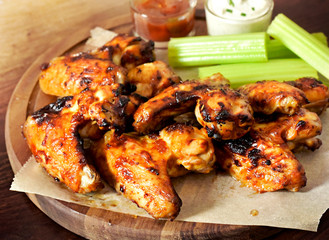 Delicious chicken wings on a wooden cutting board. Close-up shot of tasty chicken wings with perennial celery, sour cream dip and bbq sauce.