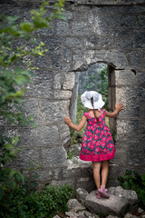 Little girl in summer dress peeking through the hole in the ancient wall
