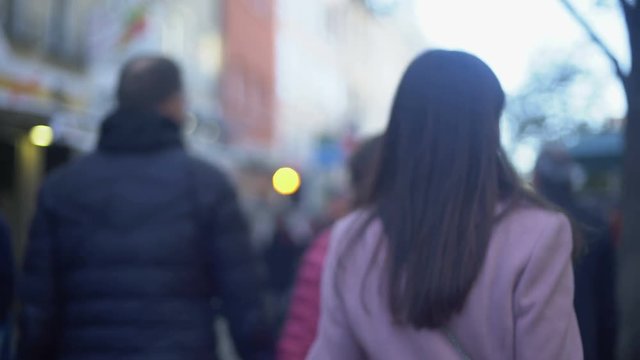 Nervous young female criminal walking on crowded street and turning around