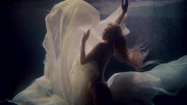 Naked woman is posing underwater with white chiffon fabric, silhouette view