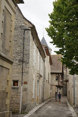 Fototapeta na wymiar Narrow street in old town in France, stone houses, two people just visible walking away, Issigeac, France