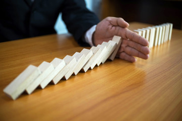 Businessman hand stops domino continuous overturned meaning that hindered business failure. Stop...