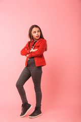 Full length photo of optimistic girl in casual smiling while standing, isolated over red background