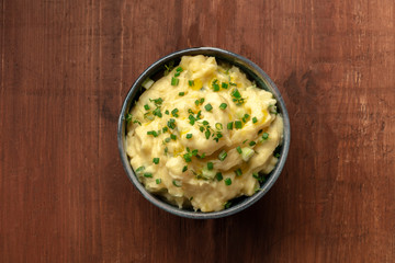 Pomme puree, an overhead photo of a bowl of mashed potatoes with herbs, shot from the top on a dark rustic wooden background with a place for text