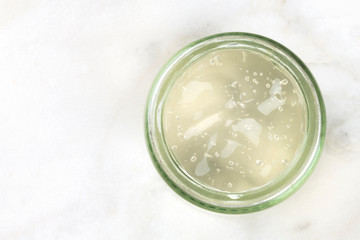 Aloe vera gel in a glass jar on a light background, shot form the top with a place for text