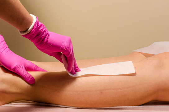 Beautician waxing a woman's leg applying a strip of material over the hot wax to remove the hairs when pulled