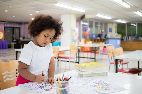 Mixed race girl, tanned skin, Curly short hair sitting, drawing and painting with concentration and intended in the library at school. In Bangkok, Thailand. Education Concept with Copy space