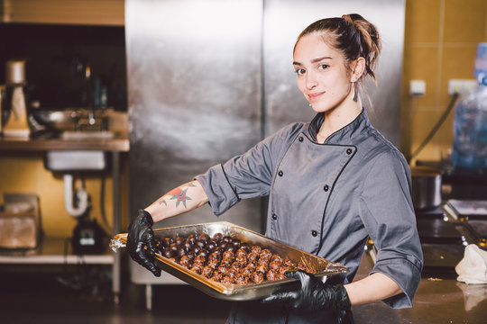 Subject profession and cooking pastry. young Caucasian woman with tattoo of pastry chef in kitchen of restaurant preparing round chocolate candies handmade truffle in black gloves and uniform