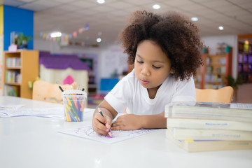 Mixed race girl, tanned skin, Curly short hair sitting, drawing and painting with concentration and intended in the library at school. In Bangkok, Thailand. Education Concept with Copy space