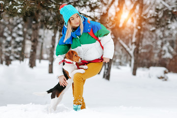 Portrait of cheerful young woman in warm stylish clothes and bagpack posing with her beagle dog in winter park. Friendship, pet and human.