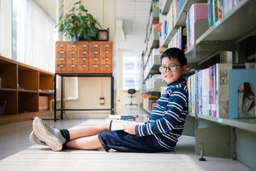 Asian Thai boy wearing glasses, long sleeves and shorts, sitting cross-legged on the floor and...