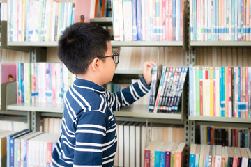 Asian Thai boy wearing glasses, long sleeves and shorts. He is choosing and picking up books on the...