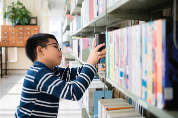 Asian Thai boy wearing glasses, long sleeves and shorts. He is choosing and picking up books on the...