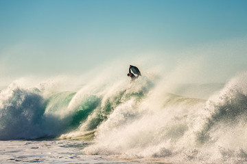 Surfer jumps a powerful and big wave at sunset