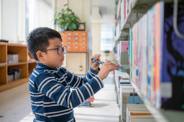 Asian Thai boy wearing glasses, long sleeves and shorts. He is choosing and picking up books on the...