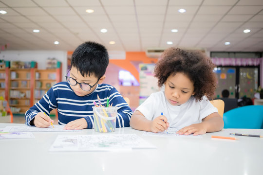 Asian Thai boy wearing glasses and Mixed race girl, tanned skin are drawing and painting with concentration and intended in the library at school. In Bangkok, Thailand. Education Concept