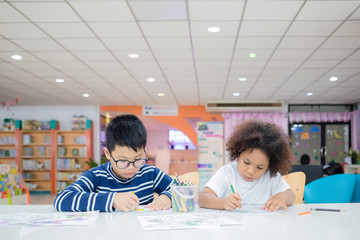 Asian Thai boy wearing glasses and Mixed race girl, tanned skin are drawing and painting with concentration and intended in the library at school. In Bangkok, Thailand. Education Concept