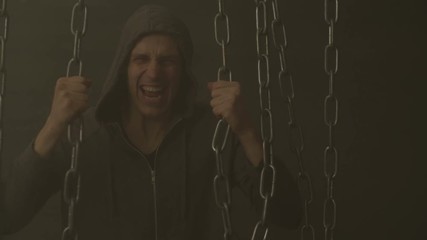Tough man in hoodie trying hard to break rusty iron chains to liberate himself from shackles of dogma and social prejudices over black background with smoke. Guy tearing chains to free his soul .