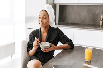 Portrait of adorable african american woman wearing housecoat, having breakfast at home