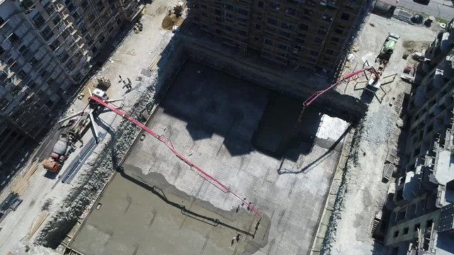 the casting of the concrete Foundation of a house. Bird's-eye view. Two concrete pumps feed the solution into an earthen pit, where workers level the concrete. Concrete is transported in a concrete mi