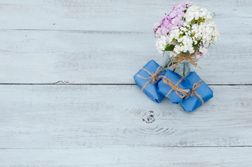 flowers in a vase and gifts on a wooden background, top view, place for text